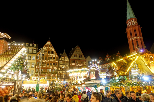Ein geschäftiger Weihnachtsmarkt in Nürnberg, Deutschland mit Menschen um geschmückte Stände, festliche Lichter, Gebäude mit Fenstern und einen Kirchturm.