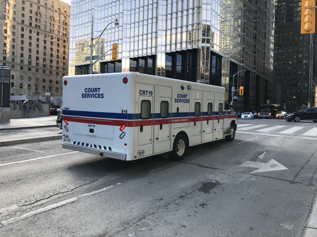 Ambulanz auf einer Stadtstra├če mit hohen Geb├Ąuden, Stra├čeninfrastruktur und Passanten, unter einem sichtbaren Himmel.