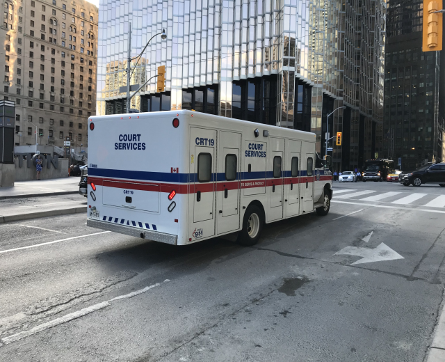 Ambulanz auf einer Stadtstra├če mit hohen Geb├Ąuden, Stra├čeninfrastruktur und Passanten, unter einem sichtbaren Himmel.