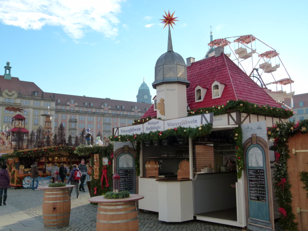 Ein geschäftiger Weihnachtsmarkt in Nürnberg, Deutschland mit Menschen um geschmückte Stände, festliche Lichter, ein Riesenrad im Hintergrund und eine Tafel mit Schrift auf der rechten Seite.