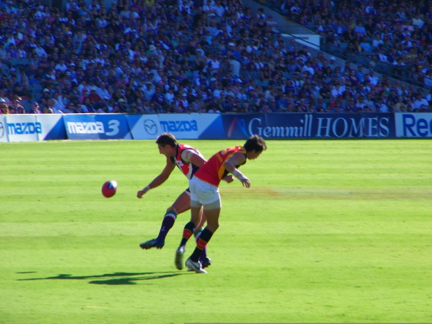 Zwei Personen in rot-weißer Kleidung stehen mit einem Ball in der Luft, w√§hrend im Hintergrund des Stadions eine Menge und Fahnen zu sehen sind.