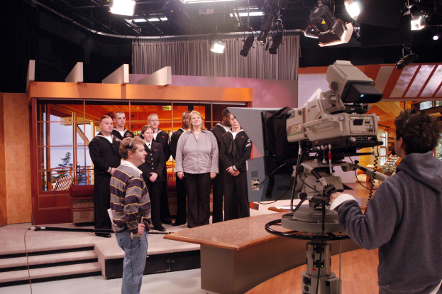 Gruppe von Menschen in einem Fernsehstudio mit einer Person, die eine Kamera hält, und Scheinwerfern an der Decke.