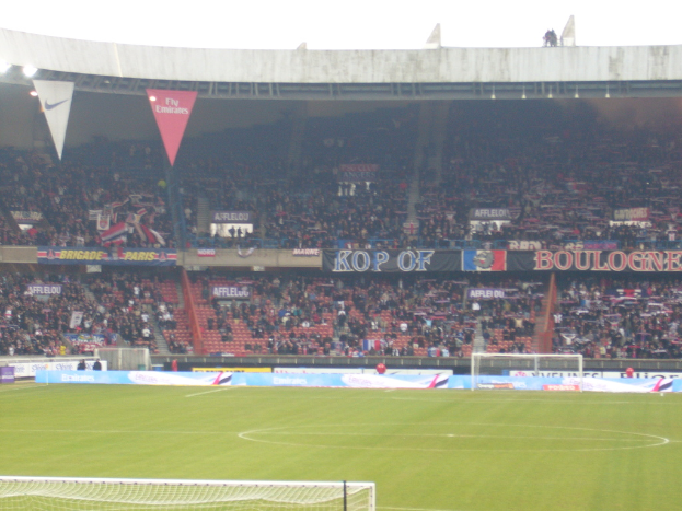 Ein Rasenstadion mit Torpfosten auf beiden Seiten, gefüllt mit Zuschauern im Hintergrund und zahlreichen Werbetafeln.