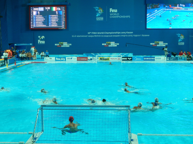 Wasserballspieler bei den FINA-Weltmeisterschaften 2016 in Kazan im Pool gegeneinander antretend, mit Zuschauern auf der linken Seite und einem Werbeschild im Hintergrund.