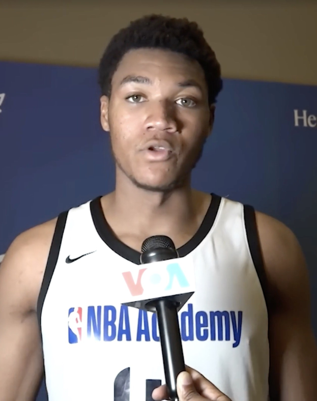 Mann in weißem Tanktop mit Mikrofon, spricht mit Medien vor Banner "NBA All-Star Game 2019"