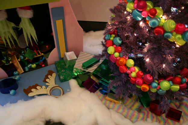 Drinnen ein geschmückter Weihnachtsbaum rechts, Geschenkboxen und Dekorationen in der Mitte, eine Hütte mit Dekorationen oben links und Baumwolle und Wolle unten.