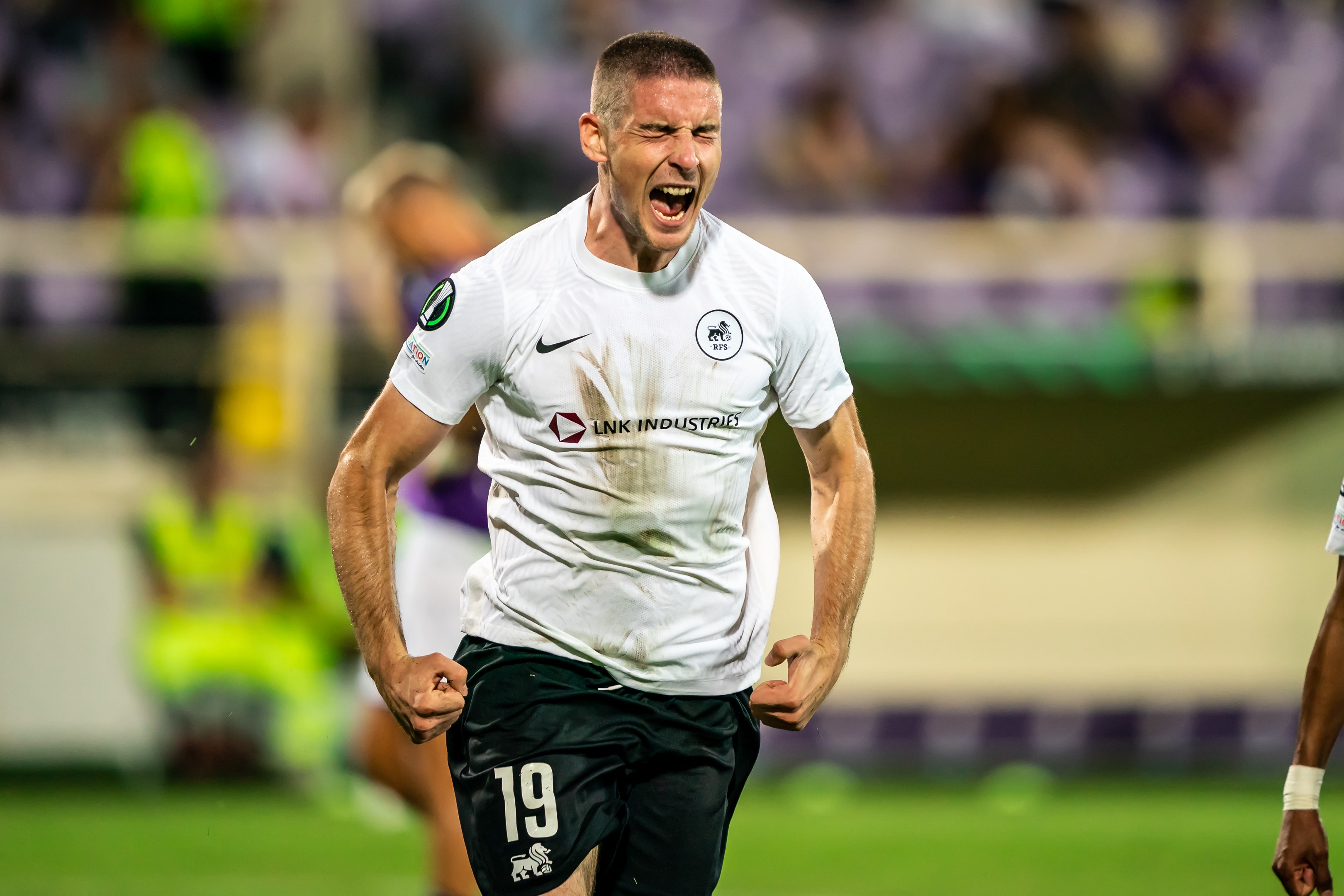 Ein Mann in weißem Hemd und schwarzen Shorts rennt auf einem Fußballfeld, umgeben von einer Gruppe von Menschen, die ein Tor während eines Matches zwischen Leeds United und Melbourne Victory feiern.