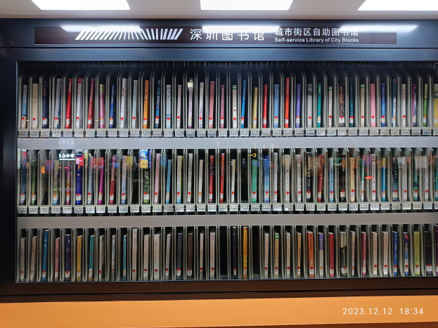 Eine gut beleuchtete Bibliothek mit hohen Bücherregalen, die mit Büchern gefüllt sind, mit einer Tafel mit Text und einem Wasserzeichen am unteren Rand, das einer Selbstbedienungsbibliothek der Stadt ähnelt.