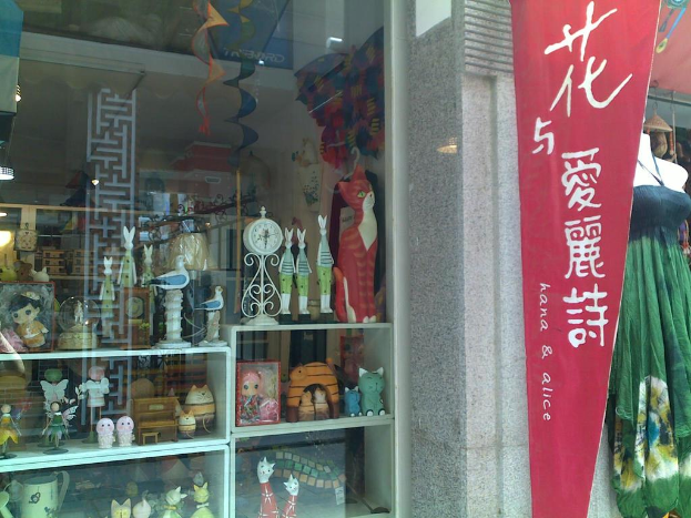 Eine Ausstellung mit verschiedenen Gegenständen, darunter ein Banner, eine Schaufensterpuppe und ein Traumfänger auf der linken Seite und Spielzeug, eine Uhr und ein Schrank durch ein Glasfenster auf der rechten Seite zu sehen.