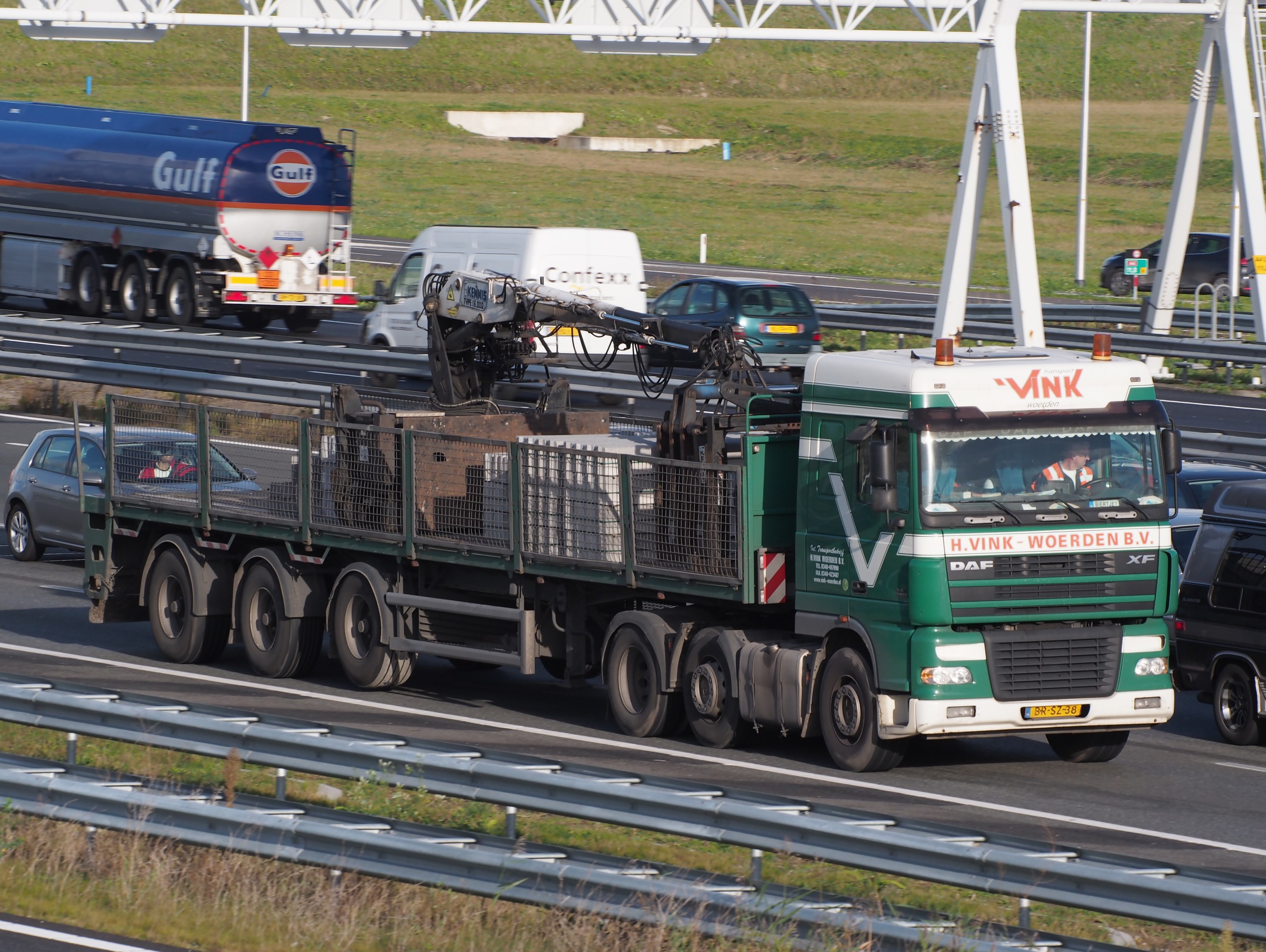 Ein großer Frachtliner-Lkw fährt auf einer Autobahn neben einer Brücke mit Geländern und Gras auf beiden Seiten, mit einem grasbewachsenen Bereich, Polen und einem klaren blauen Himmel im Hintergrund.