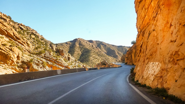 Winding road through a rocky gorge with hills on either side and a clear blue sky.