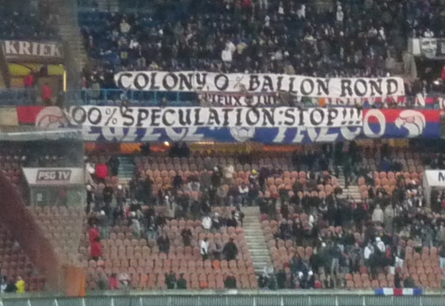 Ein Stadion voller großer Menge, Banner und Stühle, mit einem Zaun unten und einer Treppe links.