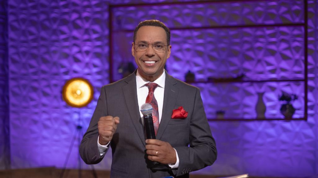 Stephen Colbert, Moderator von 'The Daily Show with Trevor Noah', steht auf einer Bühne und hält ein Mikrofon in der Hand, trägt einen Anzug und eine Brille, mit Bühnenbeleuchtung und Equipment im Hintergrund.