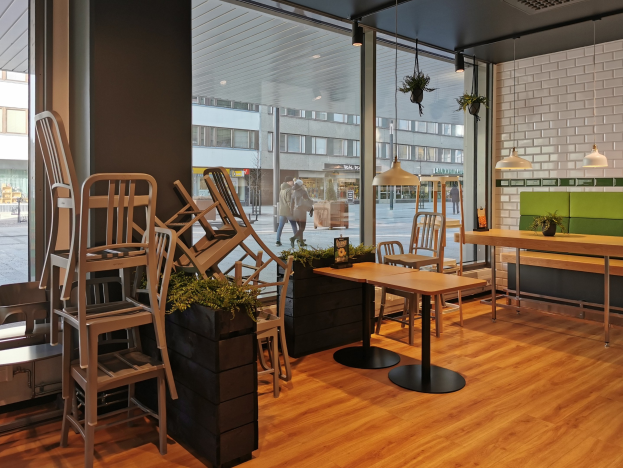 Ein Restaurant in Berlin mit Holztischen und -stühlen vor einem großen Fenster, das auf eine Straße mit Fußgängern, Gebäuden und städtischen Elementen blickt.