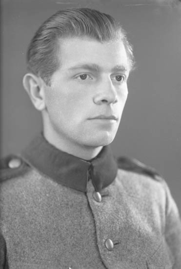 Ein Schwarz-Weiß-Foto eines Mannes in dunkler Militäruniform mit Schirmmütze, Gürtel und strenger Miene, der als erster Leutnant der Königlich Kanadischen Mounted Police identifiziert wird.