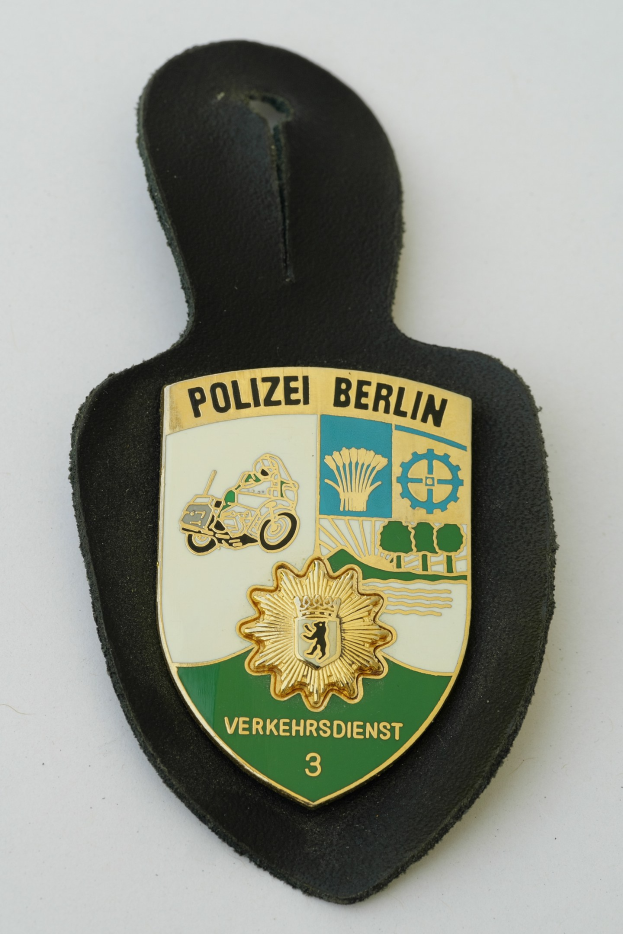 Ein schildförmiges Polizeibadged mit "Polizei Berlin" in schwarzer fetter Schrift, das einen blauen Hintergrund, einen weißen Stern und einen weißen Rand hat und auf einer Oberfläche liegt.