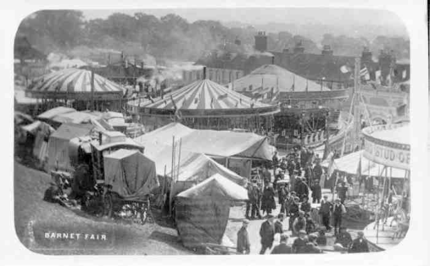 Ein altes Schwarz-Weiß-Foto einer lebhaften Karnevalszenen mit Zelten, Menschen, Wagen, Polen, Bäumen und Gebäuden im Hintergrund, beschriftet mit "Barnet Fair, London, England".