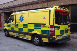 Ein Rettungswagen steht auf der Straße vor einem Backsteingebäude mit Text darauf, und ein Feuerlöscher ist auf der linken Seite des Bildes.