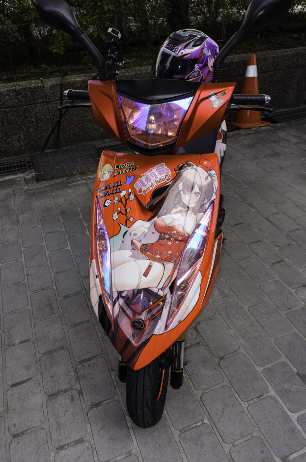 Oranger Roller auf der Straße geparkt mit einem Helm daneben, neben einem Verkehrskegel, einer Wand und Bäumen im Hintergrund.