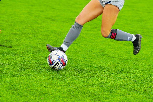 Eine Frau in einem Sportoutfit und -schuhen kickt einen Fußball auf einem saftig grünen Feld.