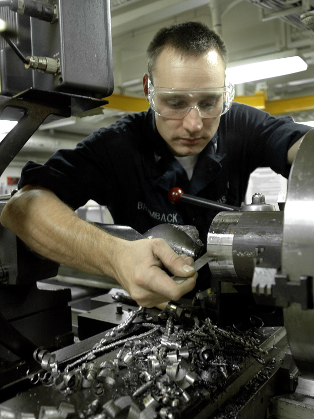 Ein Monteur mit Brille bedient eine Maschine in einer gut beleuchteten Fabrikumgebung.