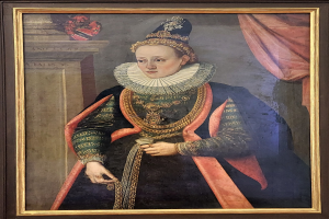 Porträt der Queen Elizabeth I. von England in königlicher Kleidung mit Krone und Tiara, das Haar zu einem Knoten gebunden, mit einem würdevollen Gesichtsausdruck, in einem Rahmen an der Wand gehängt.