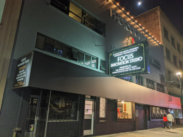 Außenansicht des Focus Innovation Studios in New York City bei Nacht, mit beleuchteten Gebäuden, Menschen auf dem Gehweg und sichtbarem Nachthimmel.