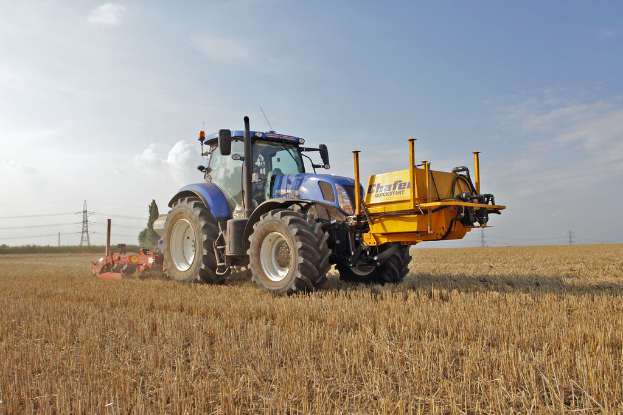 Eine Person sitzt in einem Traktor mit Strommasten und Kabeln dahinter, unter einem klaren Himmel.