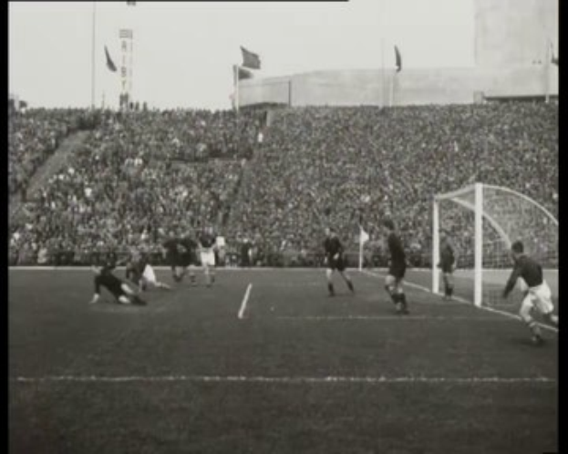 Schwarzes und weißes Foto des WM-Finales 1958 zwischen Manchester United und Liverpool, das Spieler auf dem Feld mit einem Torpfosten rechts und Zuschauern in den Rängen zeigt.