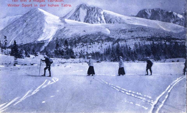 Eine Gruppe von Menschen fährt auf Skiern eine schneebedeckte Abfahrt hinunter, umgeben von Bäumen und Bergen, mit Text am unteren Bildrand.