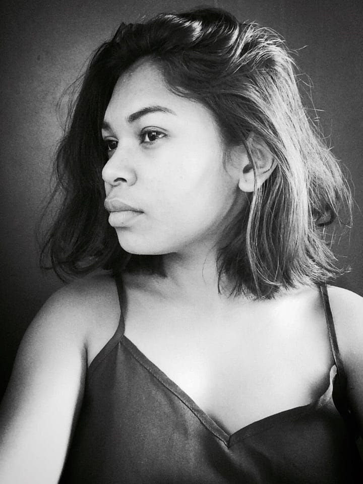 Eine selbstbewusste Frau in einem schwarzen Kleid posiert in einem Schwarz-Weiß-Foto, ihr glatter Bob und das dezente Make-up unterstreichen ihre selbstbewusste Haltung vor einer Wand.