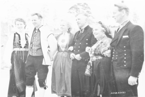 Eine Gruppe von Menschen in den 1930er Jahren, die zusammenstehen und lächeln, mit Bäumen im Hintergrund und dem Text "Bayerische Familie in den 1930er Jahren" unten.