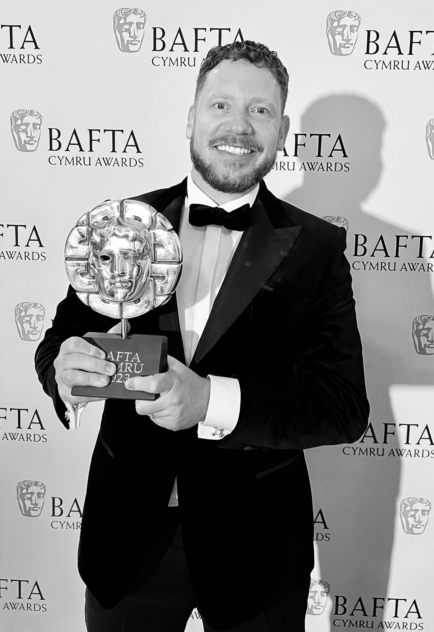 Ein Mann in einem Smoking, der eine BAFTA-Trophäe hält und vor einer Tafel mit der Aufschrift "BAFTA Awards 2018" steht.