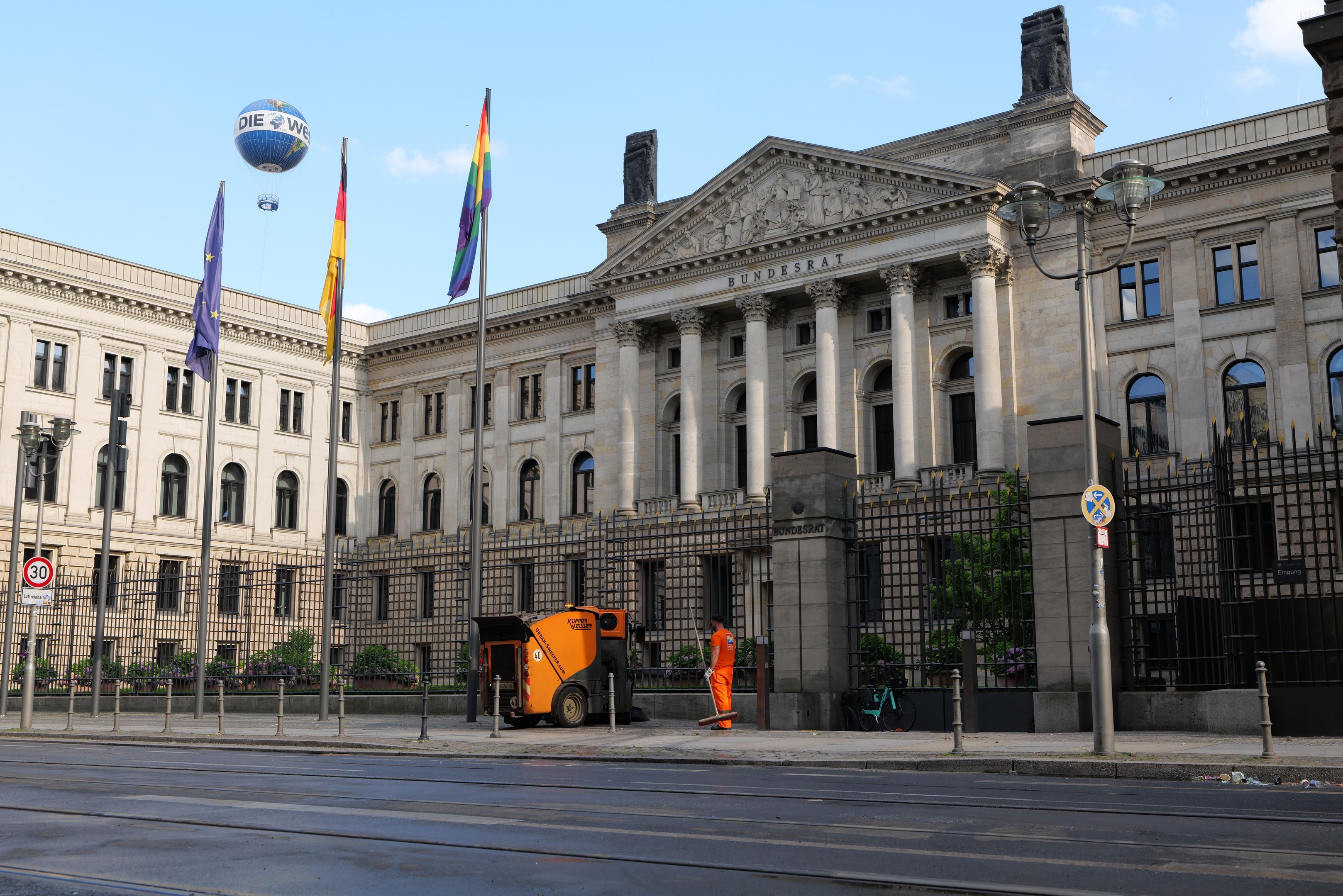 Großes modernes Gebäude mit zahlreichen Fenstern, als Bundestag in Berlin, Deutschland identifiziert, umgeben von Straßeninfrastruktur und Fußgängern unter einem bewölkten Himmel.
