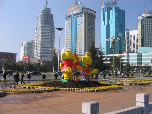 Gebäude mit Namensschildern oben, Laternenpfähle, einige Fußgänger, Luftballons, kleine Pflanzen, Bäume, Sträucher und Fahrzeuge auf der Straße.