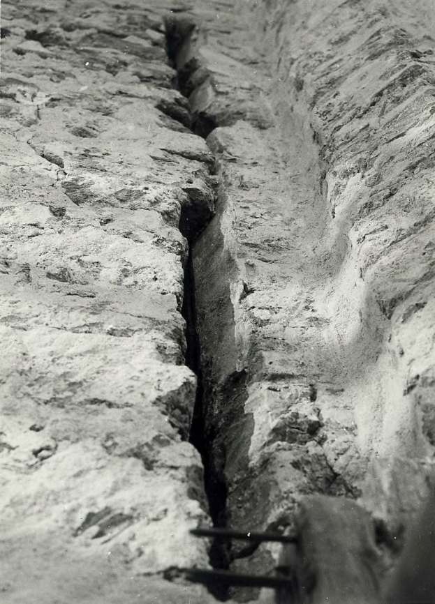 Schwarzes und weiße Foto eines großeen Risses im Boden, wahrscheinlich ein Entwässerungskanal, mit einem sichtbaren Wasserzeichen auf der linken Seite.