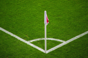 Ein Fußballfeld mit grünem Rasen und weißen Begrenzungslinien, das eine weiße Stange mit einer roten und weißen Flagge in der Mitte des Strafraums zeigt.