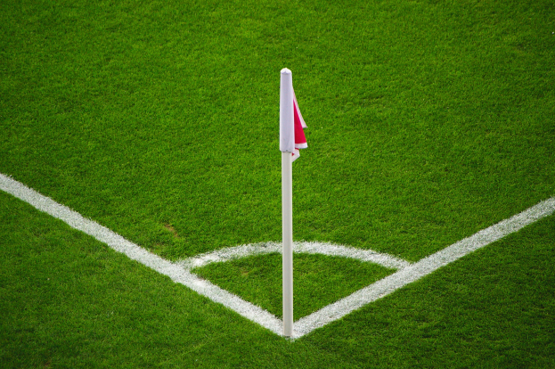 Ein Fußballfeld mit grünem Rasen und weißen Begrenzungslinien, das eine weiße Stange mit einer roten und weißen Flagge in der Mitte des Strafraums zeigt.