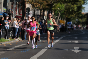 Gruppe von Menschen, die in einem Stadtmarathon laufen, mit Zuschauern und städtischen Elementen wie Bäumen, Gebäuden und einem Fahrrad im Hintergrund.