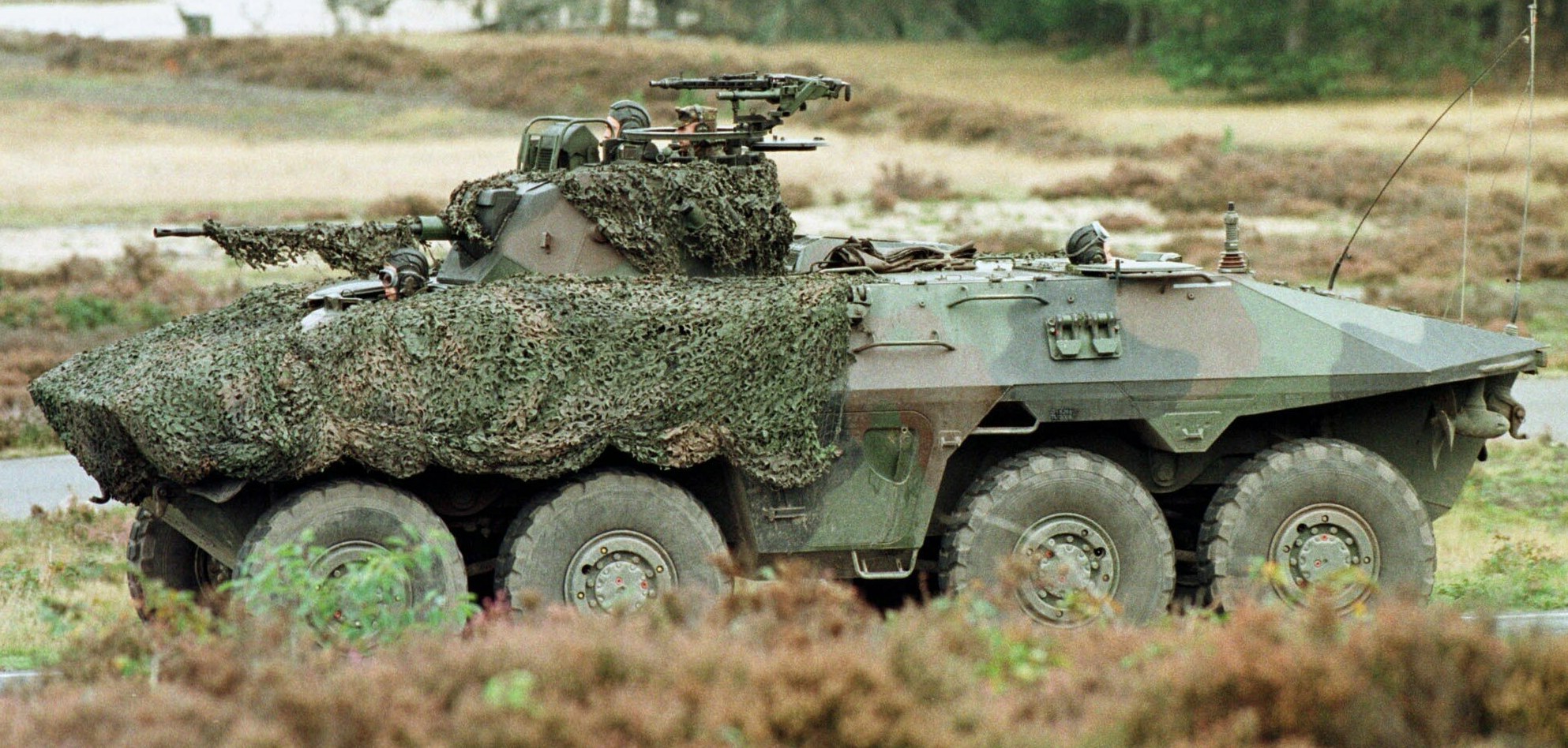 Militärpersonenwagen mit montierter großer Kanone, der auf einer Straße neben einem Wald fährt.