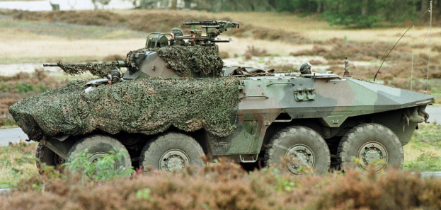Militärpersonenwagen mit montierter großer Kanone, der auf einer Straße neben einem Wald fährt.