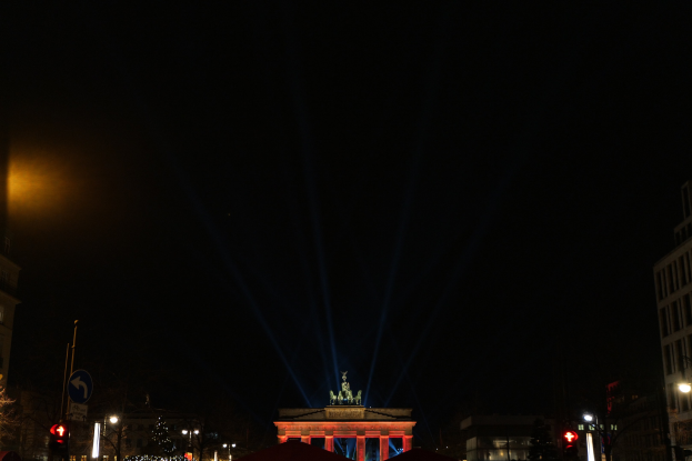 Brandenburger Tor nachts, beleuchtet von Straßenlaternen, mit umliegenden Gebäuden, Bäumen, Pfählen, Verkehrszeichen, Schildern und Zelten gegen einen dunklen Himmel.