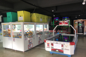 Ein vollgestopfter Arcade-Raum mit verschiedenen Arcade-Spielen, einer beleuchteten Decke und einem sichtbaren Boden.