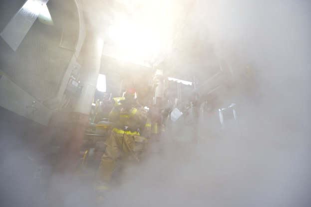 Feuerwehrleute in Schutzausrütstärbeiten in einem raucherfüllten Raum mit verstreuten Gegenständen.