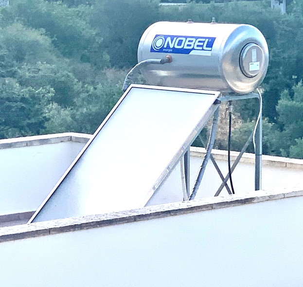 Eine Solaranlage mit einem auf dem Dach eines Gebäudes montierten Speicher, vor einem Hintergrund aus Bäumen.