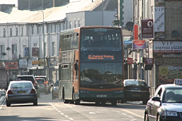 Eine Straße mit Autos und einem Bus vor Gebäuden mit Wänden, Fenstern, Tellern und Dächern, geschmückt mit Plakaten und Bannern, mit einem Laternenmast.
