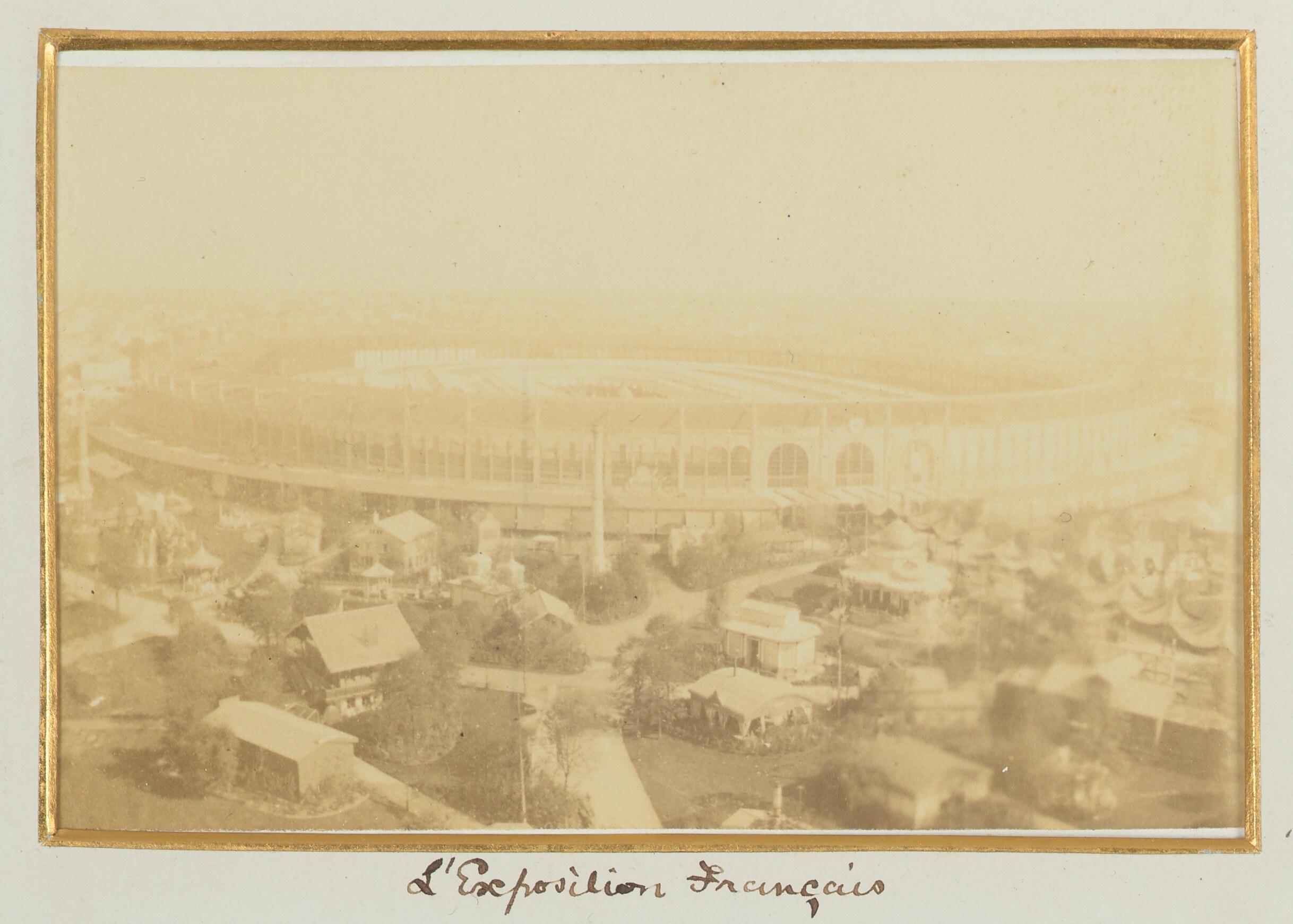 Altes Schwarz-Weiß-Foto eines Stadions, umgeben von Stadtgebäuden, Bäumen und Strommasten, mit Text unten.