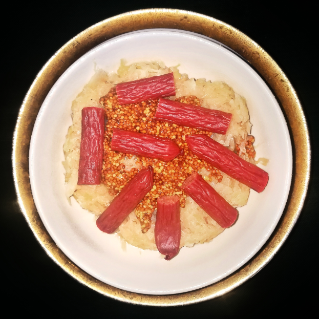 Ein weißer Teller mit einem Bett aus weißem Reis, bedeckt mit einer würzigen Sauce, garniert mit Sauerkraut und ein paar Würstchen.