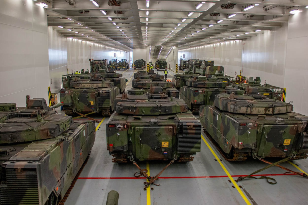 Ein grosser Militaraerraum mit zahlreichen Tanks in einer ordentlichen Reihe, beleuchtet von Deckenleuchten.