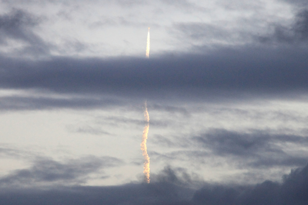 Ein Düsenflugzeug fliegt durch einen bewölkten Himmel und hinterlässt eine Rauchspur darunter.